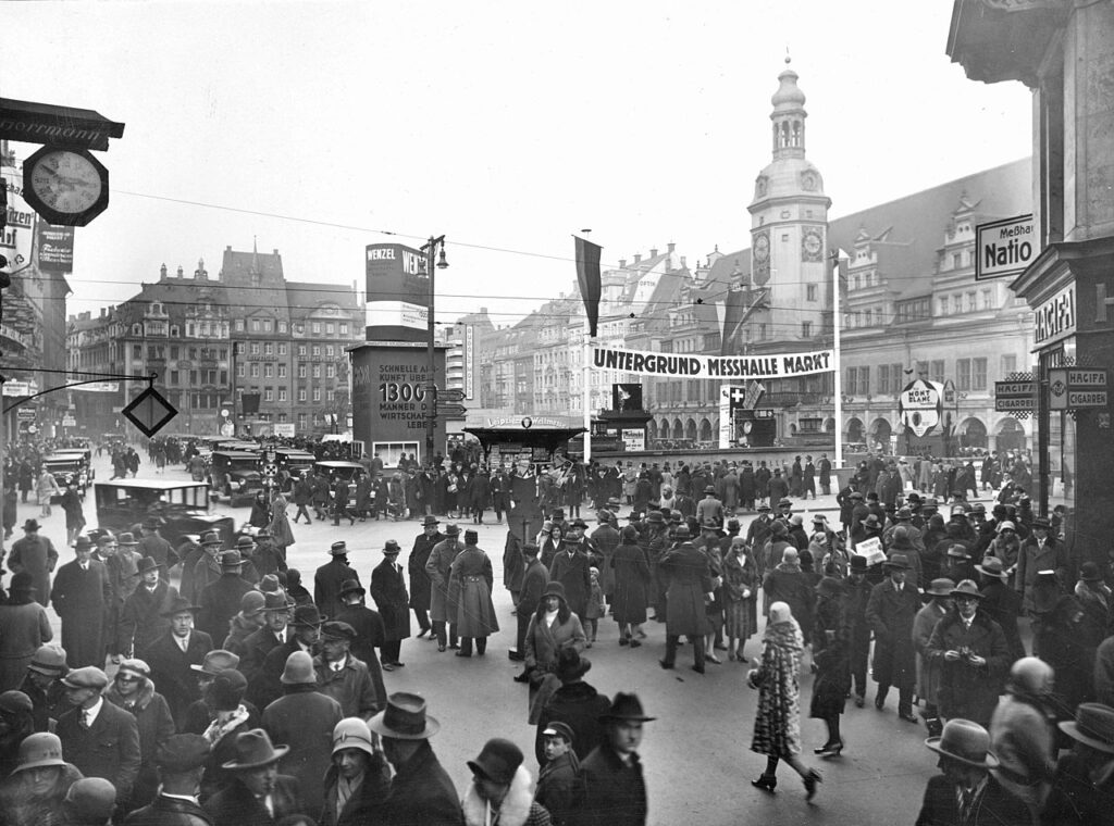 Leipzig, Markt um 1927 - von Peterstraße in Blickrichtung Norden; mit Markt 1-7, Altes Rathaus, Untergrundmessehalle; Ansicht von der Peterstraße während der Messe, zahlreiche Passanten, Werbung, Zeitungskiosk, Personenkraftwagen / <a href="https://commons.wikimedia.org/wiki/File:StadtAL_0563_BA_1977_1326.jpg">Stadtarchiv Leipzig</a>, <a href="https://creativecommons.org/licenses/by-sa/4.0">CC BY-SA 4.0</a>, via Wikimedia Commons