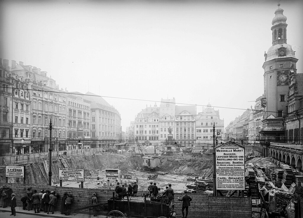 Leipzig, Markt um 1924 - Baustelle der Untergrundmessehalle in Blickrichtung Norden - mit Bautafeln, Altes Rathaus, Alte Waage, Siegesdenkmal und Geschäften: Engel-Apotheke, Seiden-Gross, Leipziger Lebensversicherungs-AG / <a href="https://commons.wikimedia.org/wiki/File:StadtAL_0563_BA_1982_14104.jpg">Stadtarchiv Leipzig</a>, <a href="https://creativecommons.org/licenses/by-sa/4.0">CC BY-SA 4.0</a>, via Wikimedia Commons